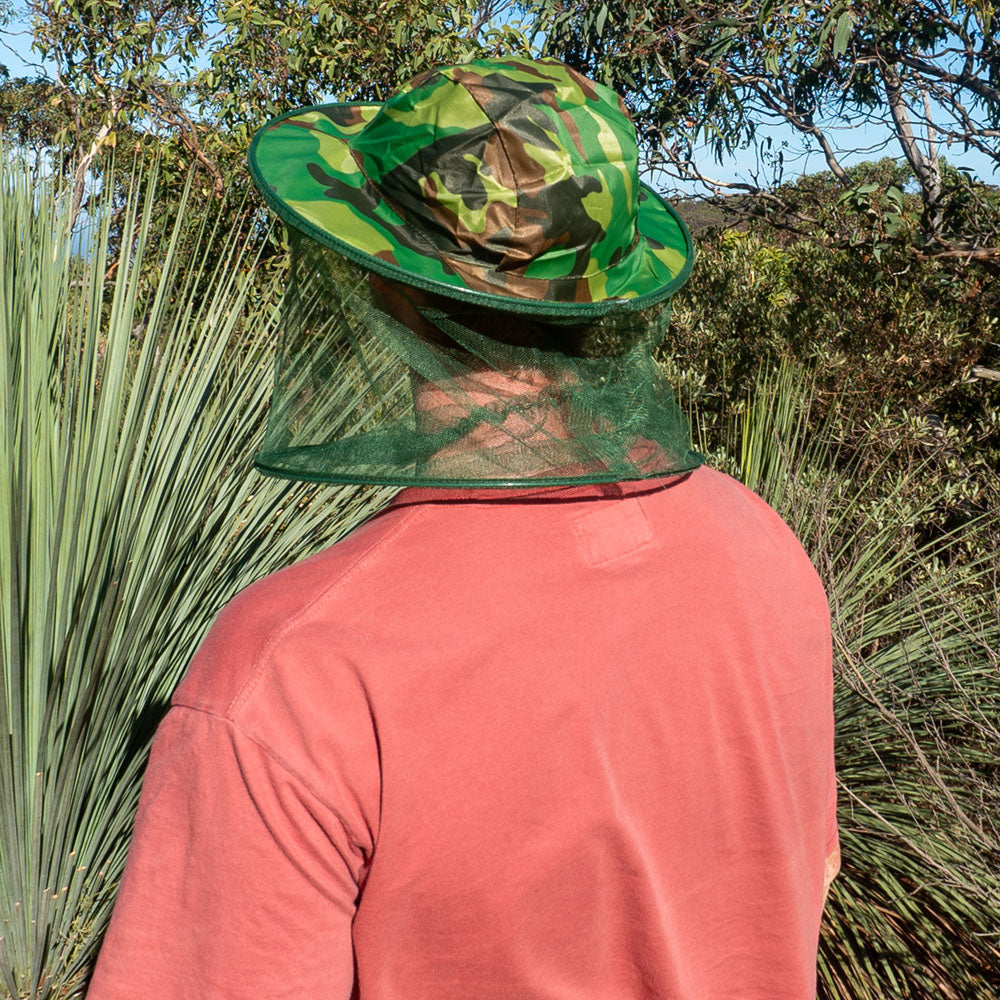 Person wearing camouflage brim hat with mosquito head net for insect protection while hiking in bushland