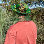 Person wearing camouflage brim hat with mosquito head net for insect protection while hiking in bushland