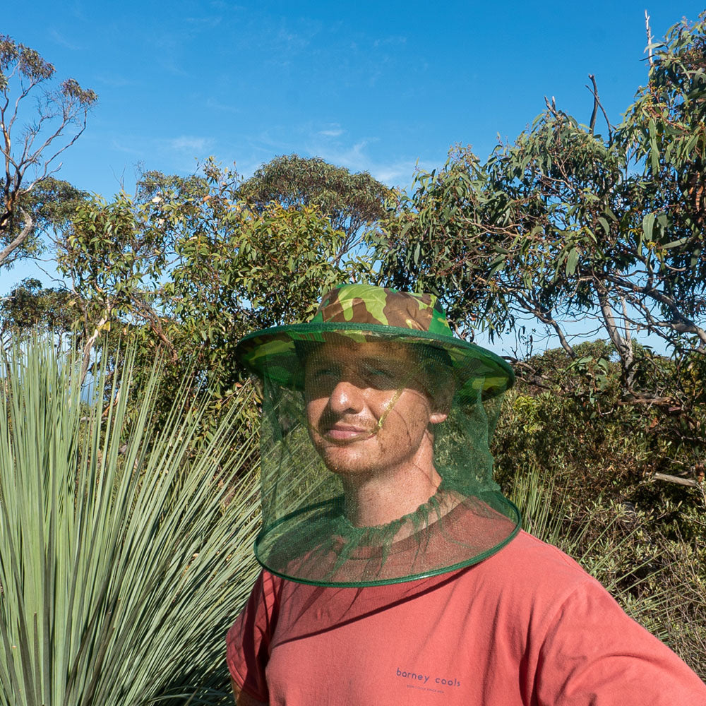 Person wearing camouflage brim hat with mosquito head net for insect protection.