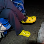 Person wearing yellow off-road clogs with socks while sitting by a campfire at night.