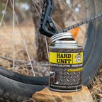  Cold Patch Solution Rubber Cement can with open lid, placed beside a bike wheel for tyre repair in outdoor setting.
