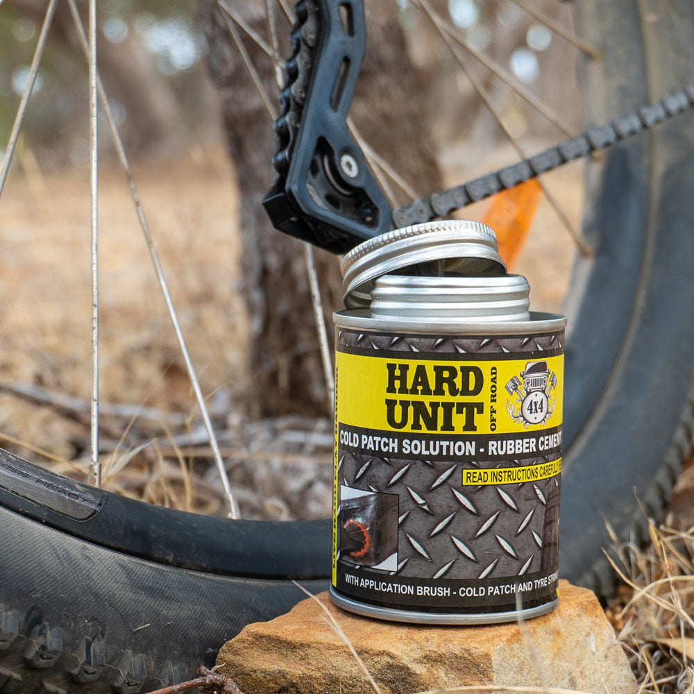  Cold Patch Solution Rubber Cement can with open lid, placed beside a bike wheel for tyre repair in outdoor setting.