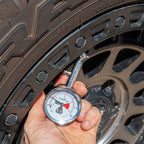 Hand holding a dial tyre pressure gauge to check air pressure on a 4WD tyre