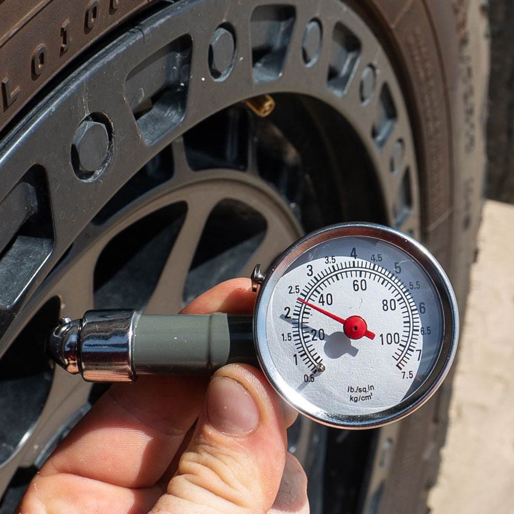 Hand holding a dial tyre pressure gauge to check air pressure on a 4WD tyre