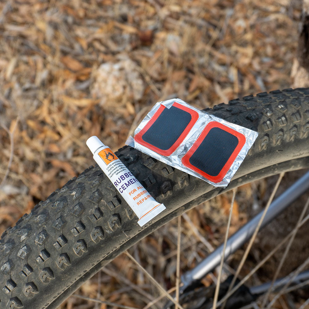 Cold patches kit with rubber cement and adhesive repair patches resting on rear wheel of a bicycle, ideal for fixing punctured bike tubes