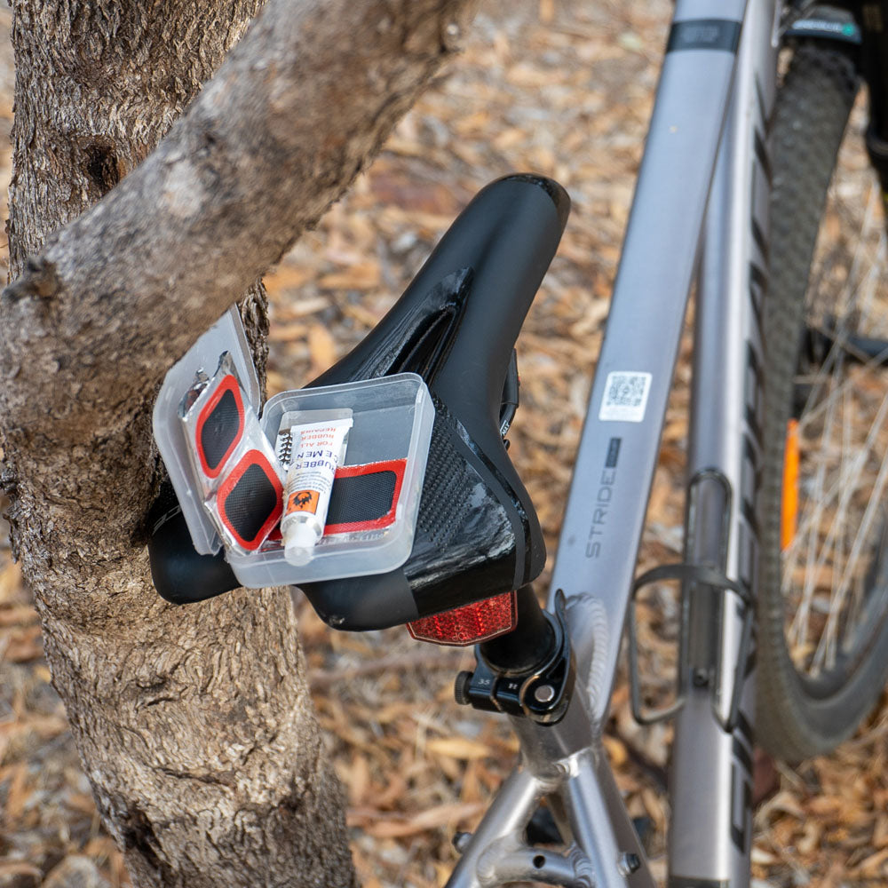 Cold patches kit with rubber cement and adhesive repair patches resting on seat of a bicycle, ideal for fixing punctured bike tubes