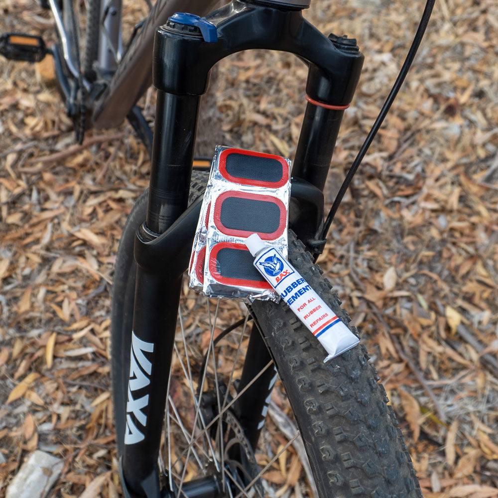 Cold patches kit with rubber cement and adhesive repair patches resting on rear wheel of a bicycle, ideal for fixing punctured bike tubes