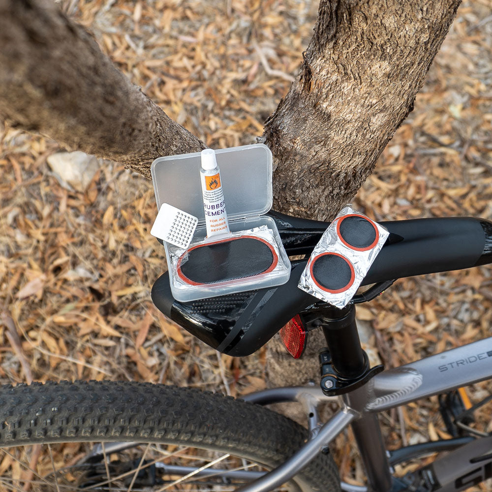 Cold patches kit with rubber cement and adhesive repair patches resting on seat of a bicycle, ideal for fixing punctured bike tubes