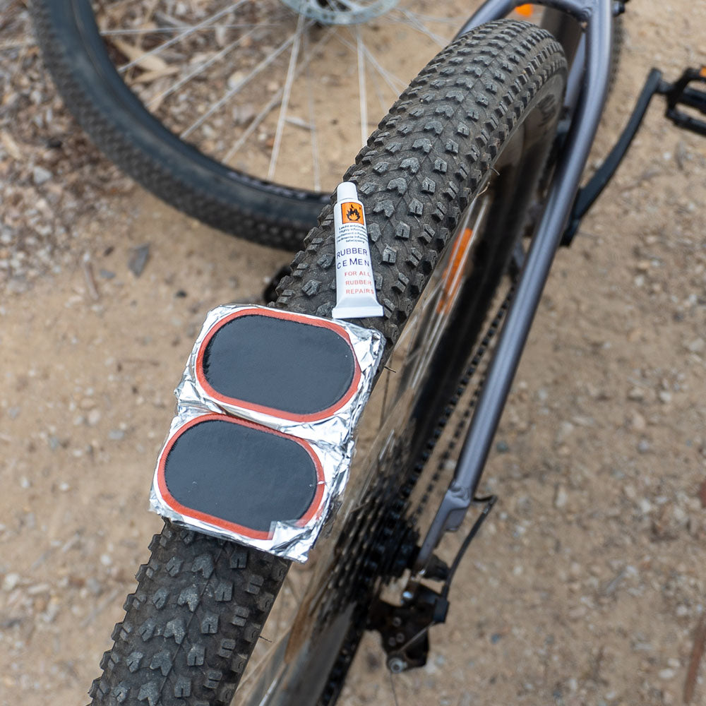 Cold patches kit with rubber cement and adhesive repair patches resting on rear wheel of a bicycle, ideal for fixing punctured bike tubes
