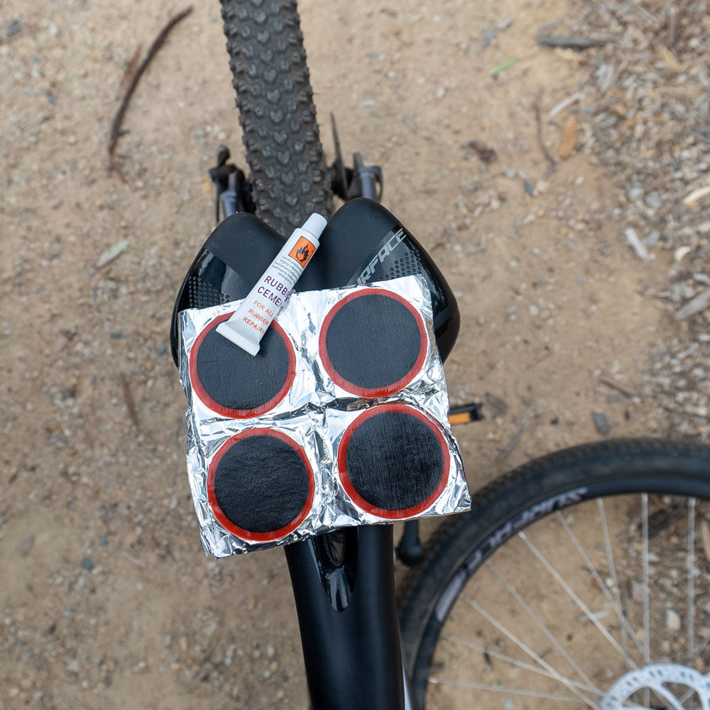Cold patches kit with rubber cement and adhesive repair patches resting on rear wheel of a bicycle, ideal for fixing punctured bike tubes.