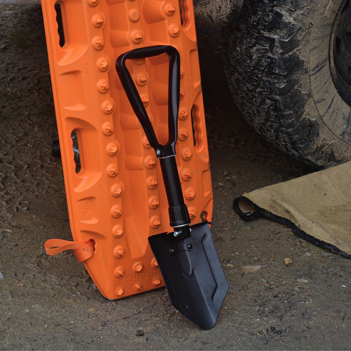 Folding spade leaning against an orange recovery track next to a muddy 4WD tyre.