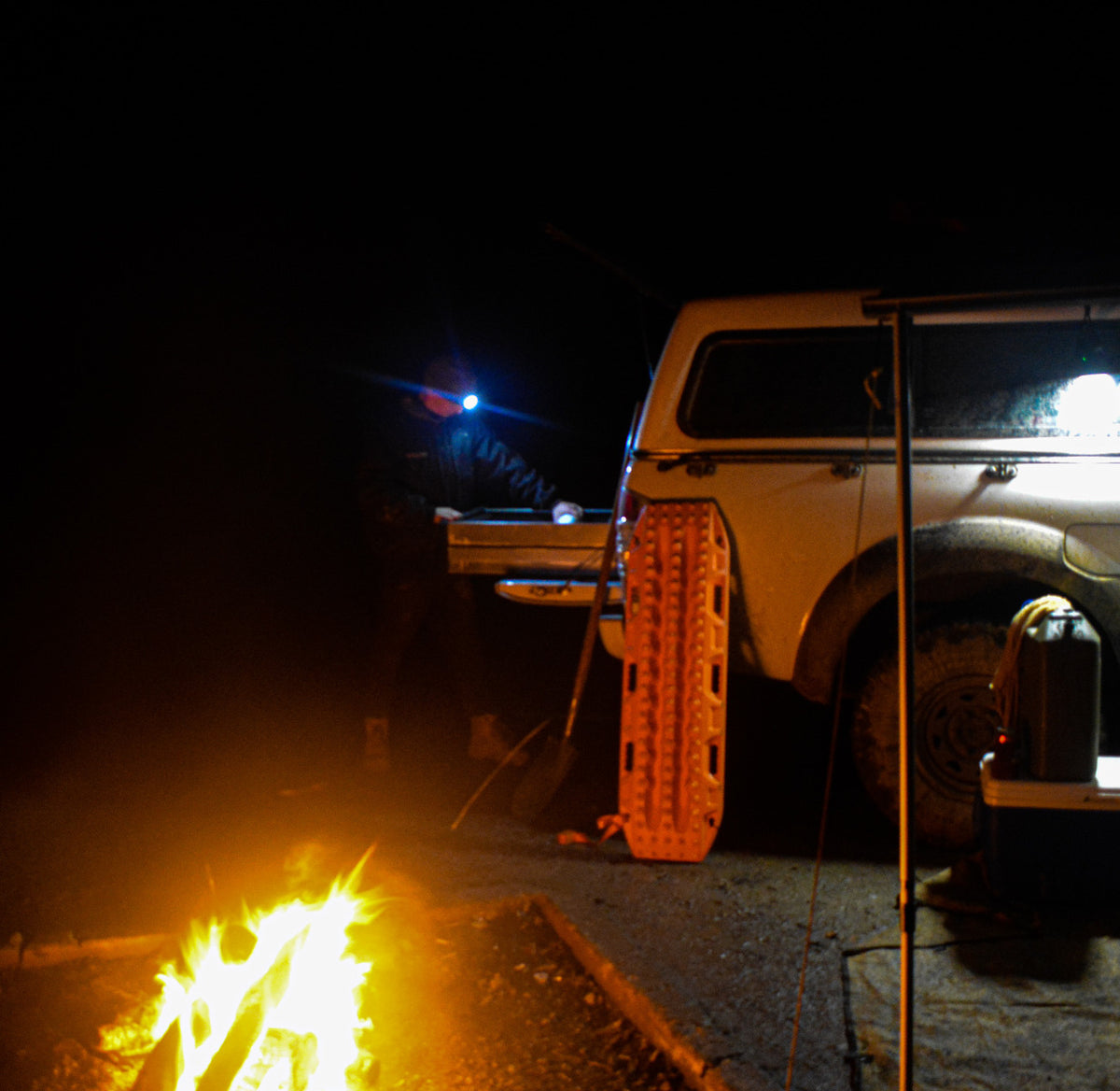 Person wearing LED beanie headlamp while camping at night, working beside a 4WD with campfire.