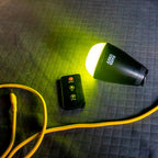 LED camping light with insect repellent glow, remote control, and yellow power cable on quilted surface.