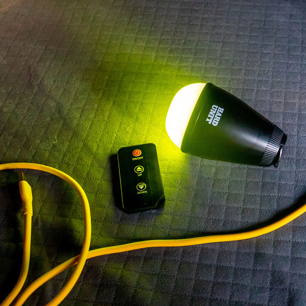 LED camping light with insect repellent glow, remote control, and yellow power cable on quilted surface.