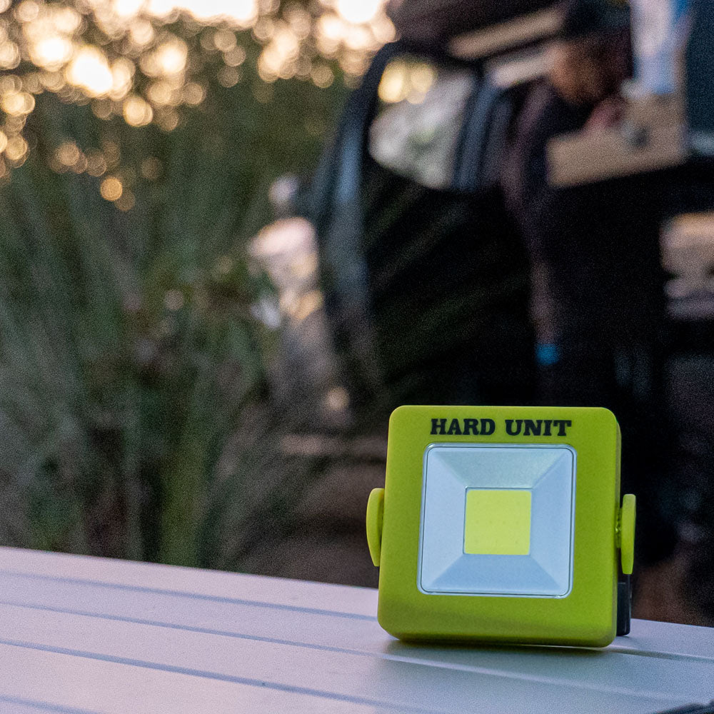Square LED work light placed on outdoor table at dusk, ideal for camping, 4WD setups, and portable task lighting.