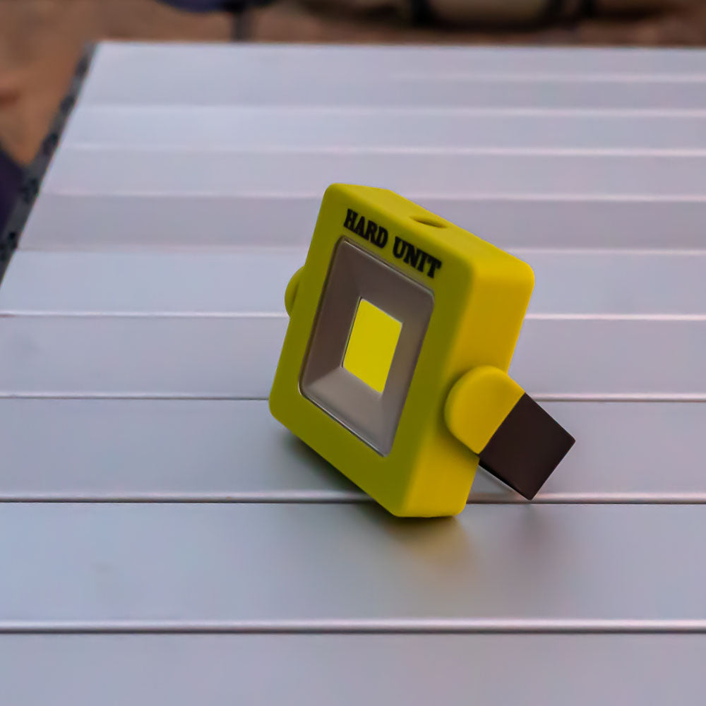 Square LED light placed on camping table for portable outdoor lighting.
