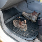 Rubber mud mats in vehicle footwell with dirty work boots, designed to trap dirt and protect interior flooring.