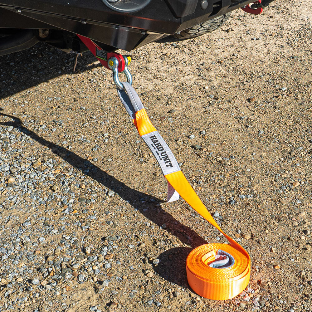 Orange snatch strap attached to 4WD recovery point on gravel surface