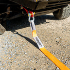 Orange snatch strap connected to 4WD recovery hitch on gravel terrain.