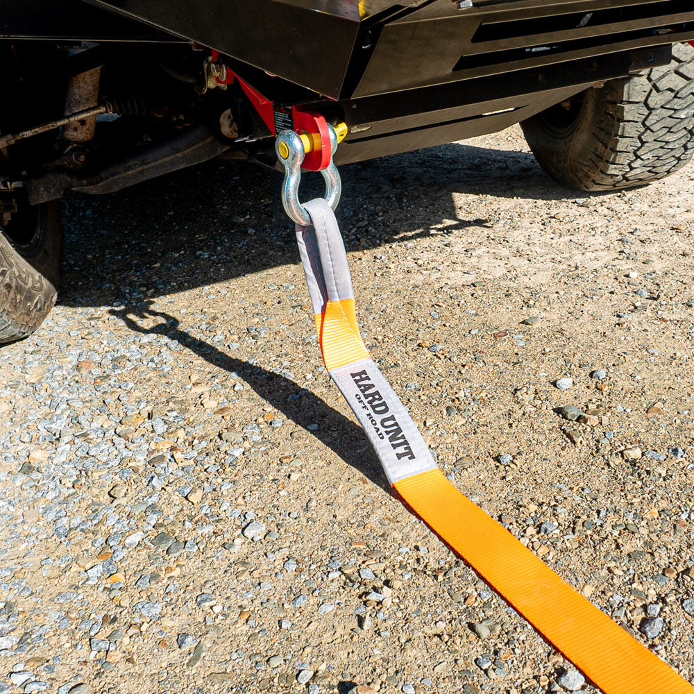Orange snatch strap connected to 4WD recovery hitch on gravel terrain.