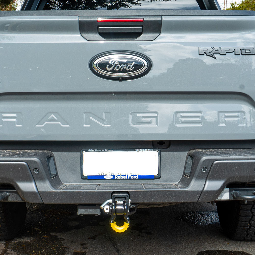 Black tow hitch receiver with mounted bow shackle and yellow isolator, attached to vehicle.