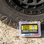 Hard Unit branded tubeless tyre repair kit with 56 pieces in a clear plastic case, placed beside a 4WD tyre on gravel.