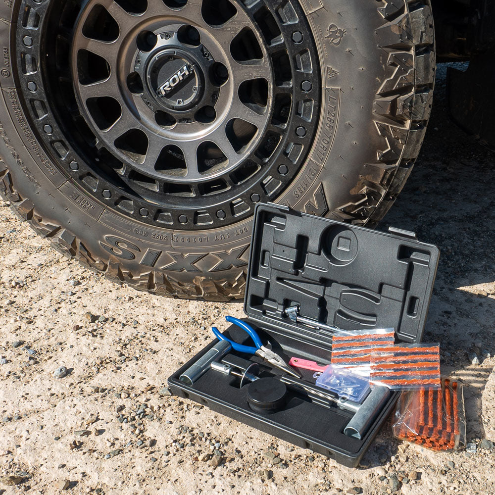 60-piece tubeless tyre repair kit in an open black hard case with pliers, repair tools, and tyre plugs, placed on gravel next to a 4WD tyre