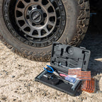 60-piece tubeless tyre repair kit in an open black hard case with pliers, repair tools, and tyre plugs, placed on gravel next to a 4WD tyre