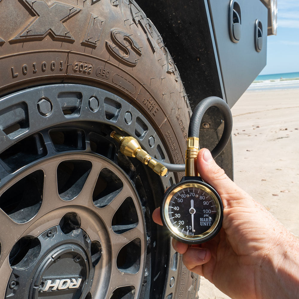 Tyre deflator gauge kit in use on a 4WD tyre at the beach, displaying PSI reading for accurate pressure adjustment.