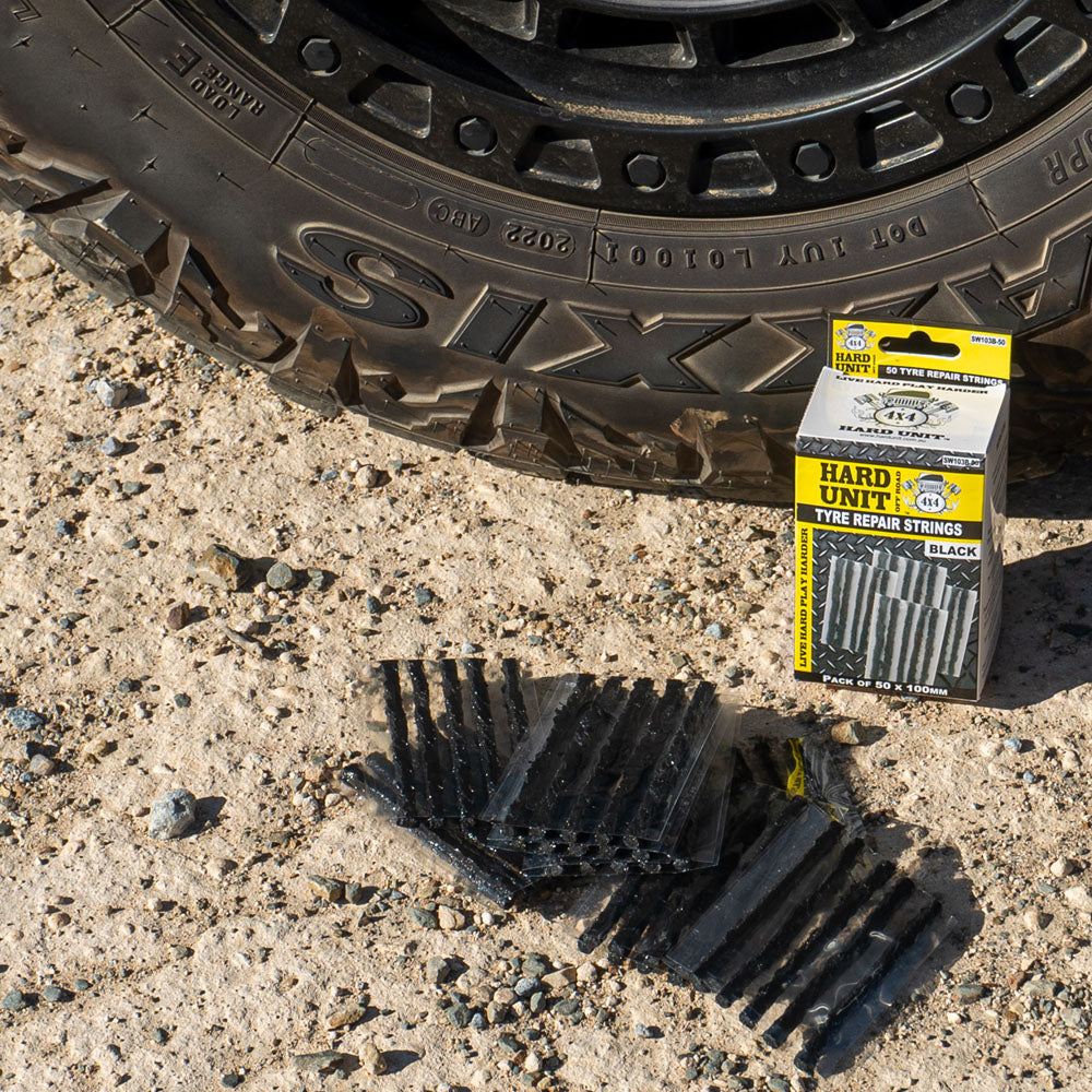 Tyre repair strings laid out on gravel next to a 4WD tyre and Hard Unit packaging, used for emergency puncture repairs.