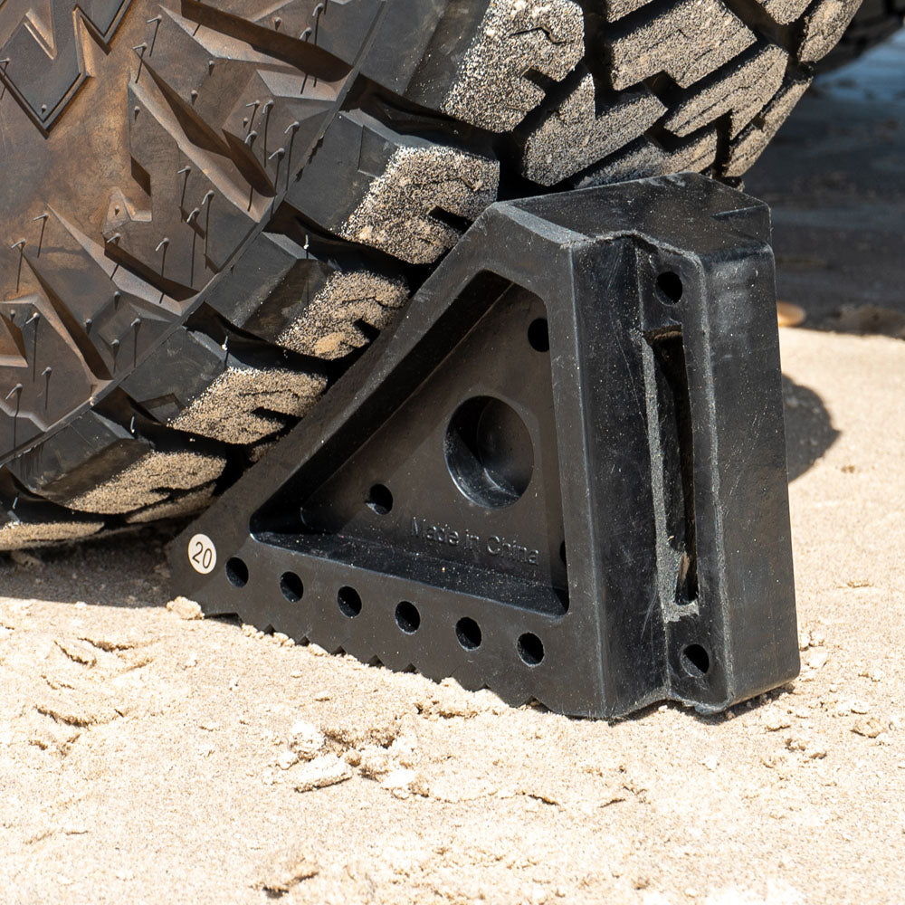 Small solid rubber wheel chock in use under a vehicle tyre on sand, providing stability
