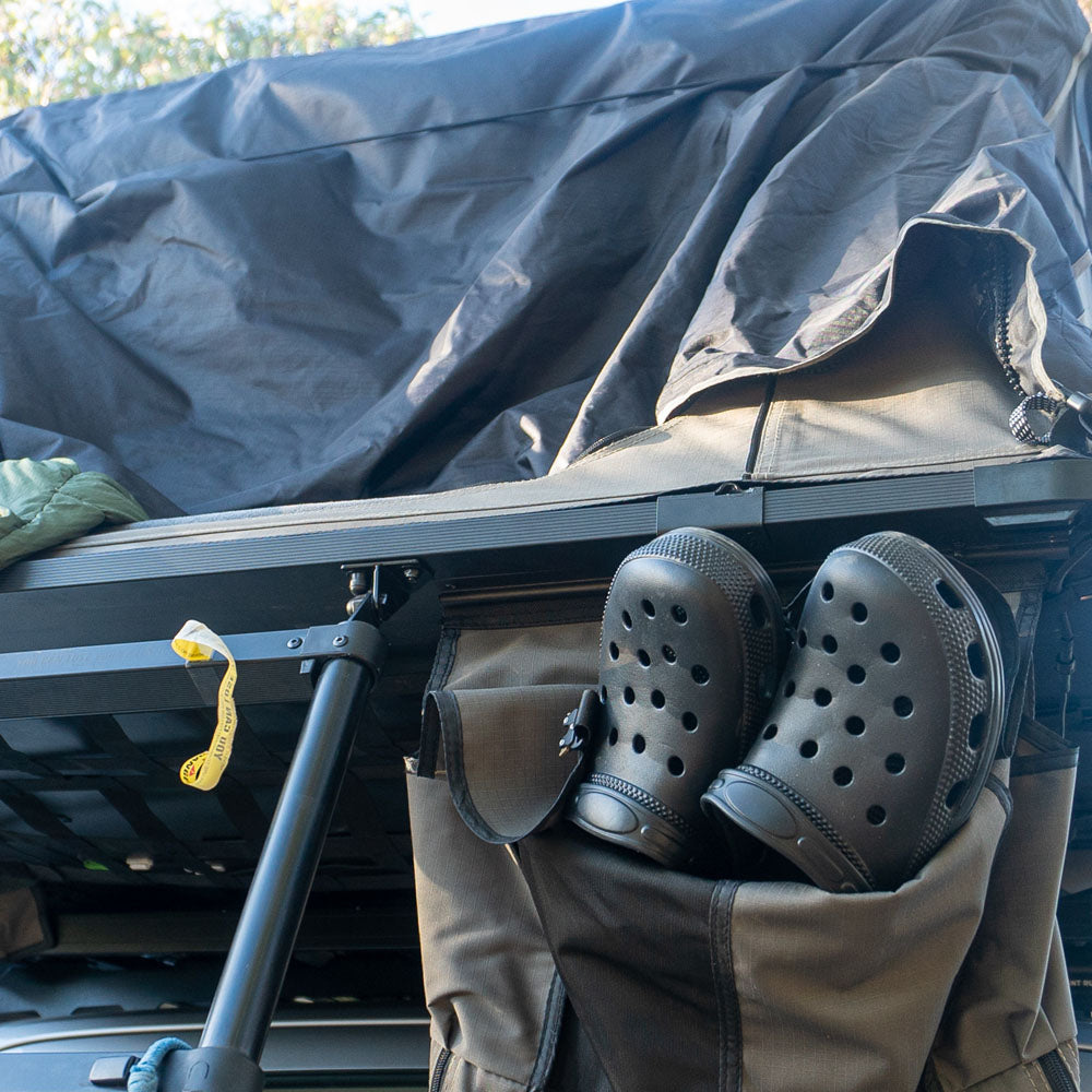Black off-road clogs stored in a rooftop tent gear pocket, ideal for camping and outdoor use.
