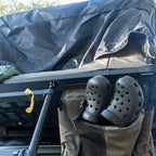 Black off-road clogs stored in a rooftop tent gear pocket, ideal for camping and outdoor use.